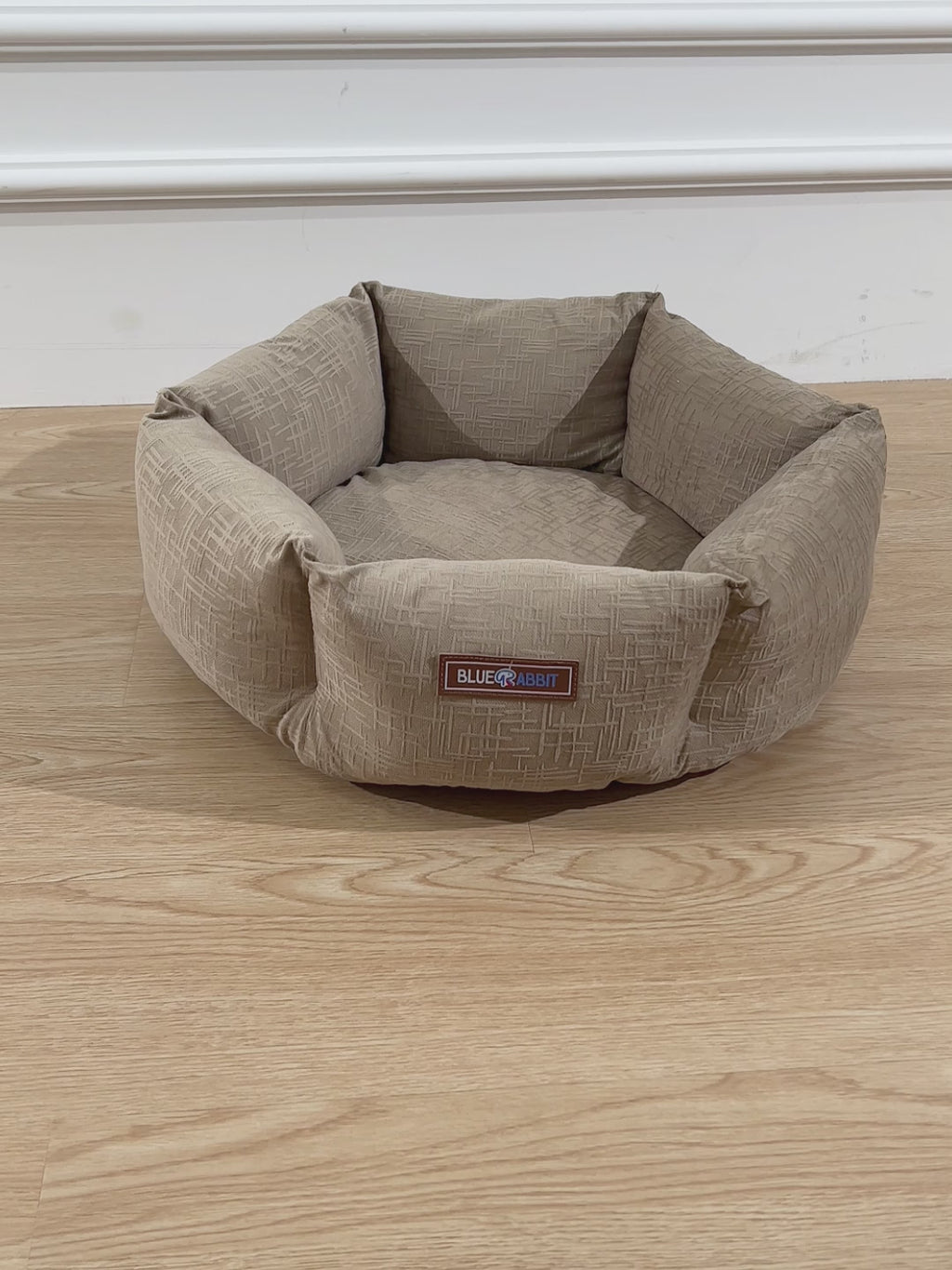 Beige pet bed with a brand label on a wooden floor