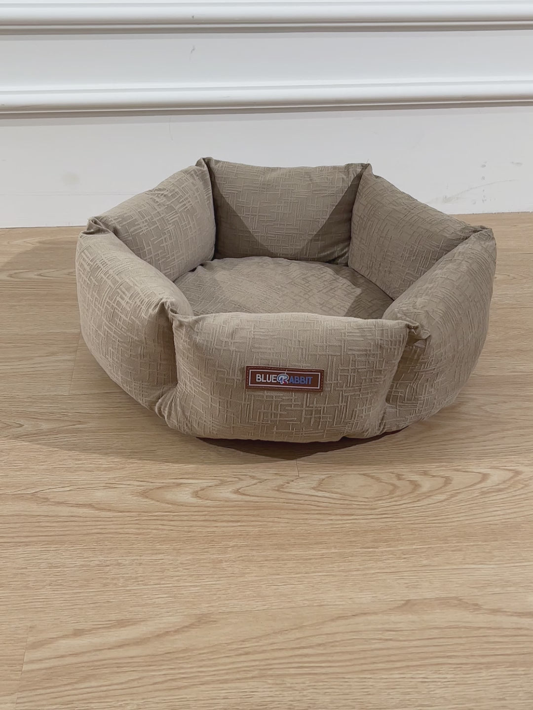 Beige pet bed with a brand label on a wooden floor