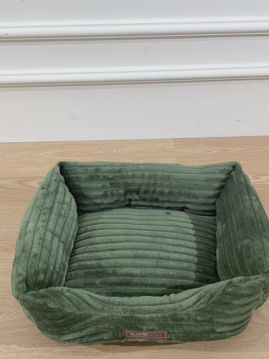 Pink pet bed on a wooden floor with a visible brand label.