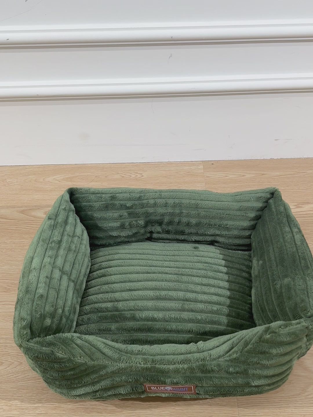 Pink pet bed on a wooden floor with a visible brand label.