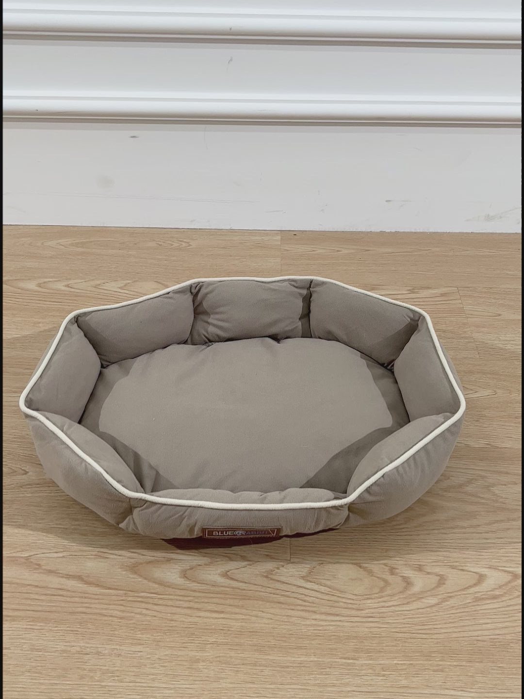 Hexagonal pet bed on a wooden floor with a brand label.