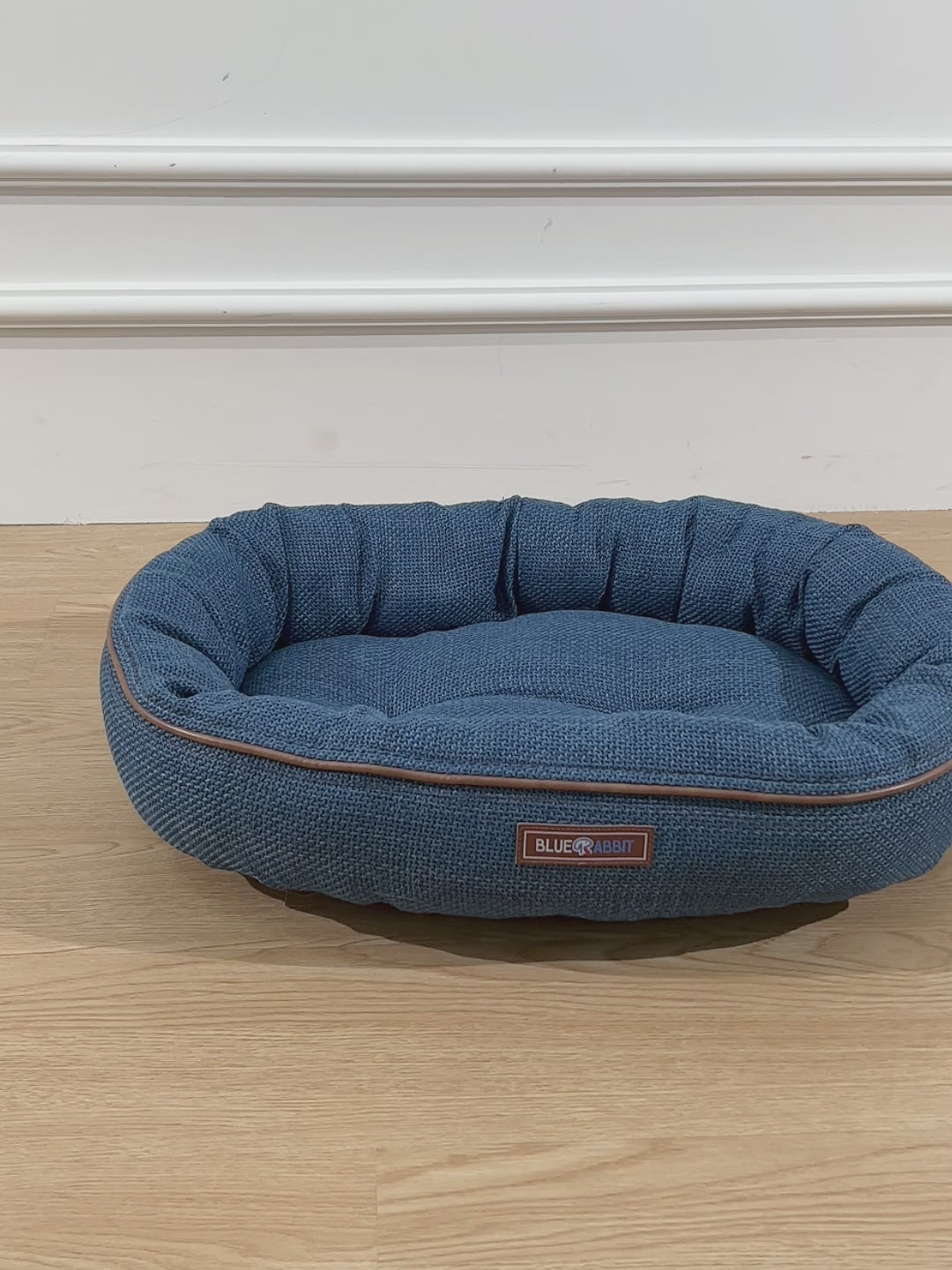 Blue pet bed on a wooden floor with a blurred background