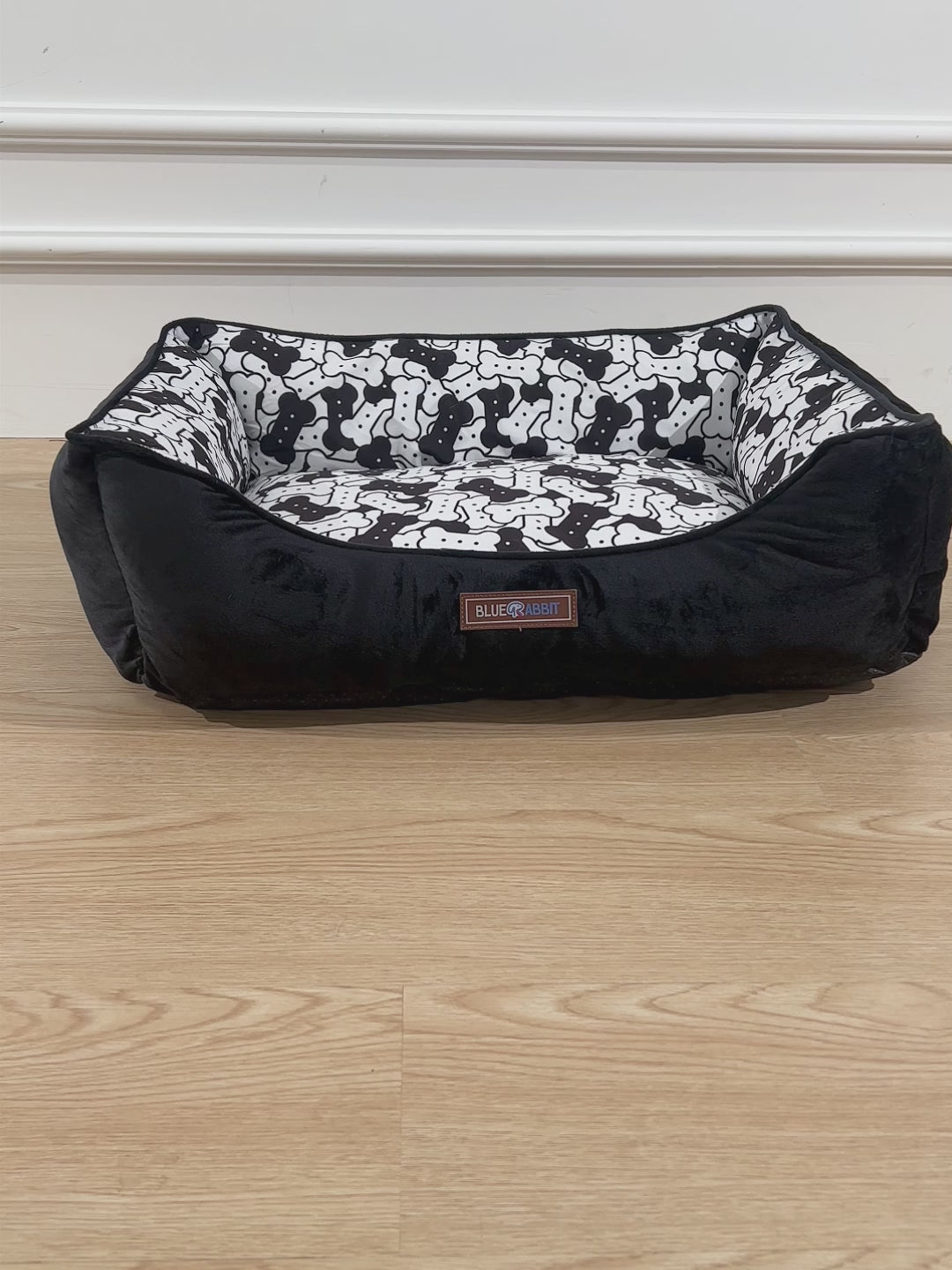 Black pet bed with white pattern on a wooden floor