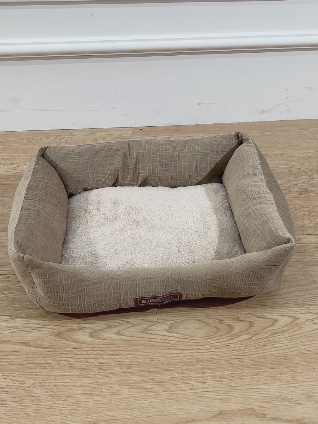 Beige_pet_bed_with_a_brand_label_on_a_wooden_floor
