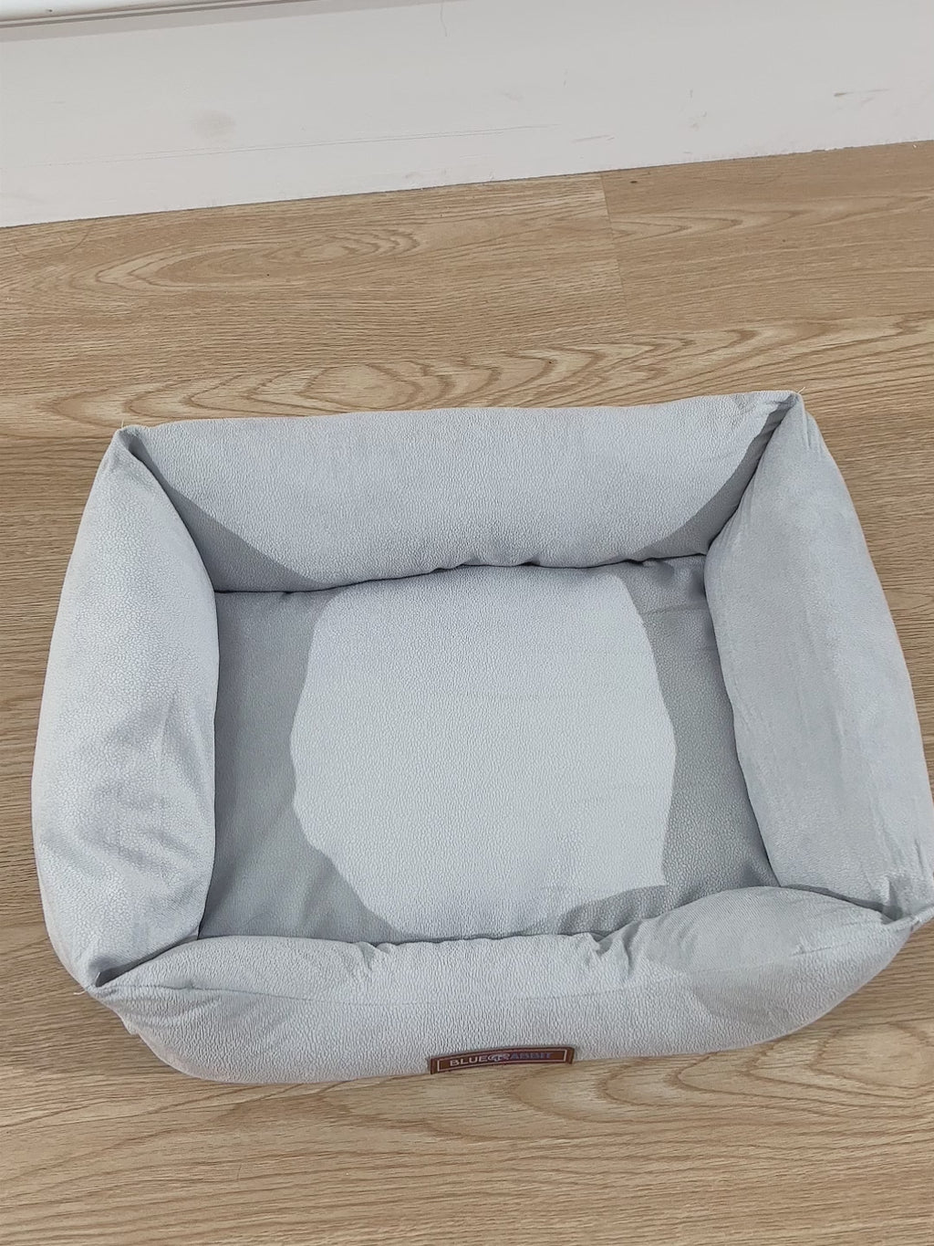 Gray pet bed on a wooden floor with a wooden cabinet in the background